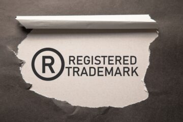 Male hand showing R-Registered trademark on wooden block. Business law